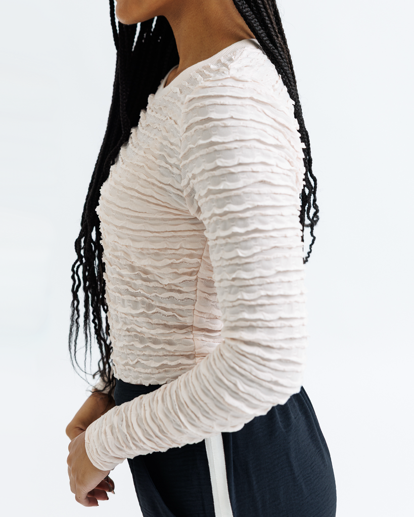 Woman wearing a cream textured long-sleeve top on a light gray background