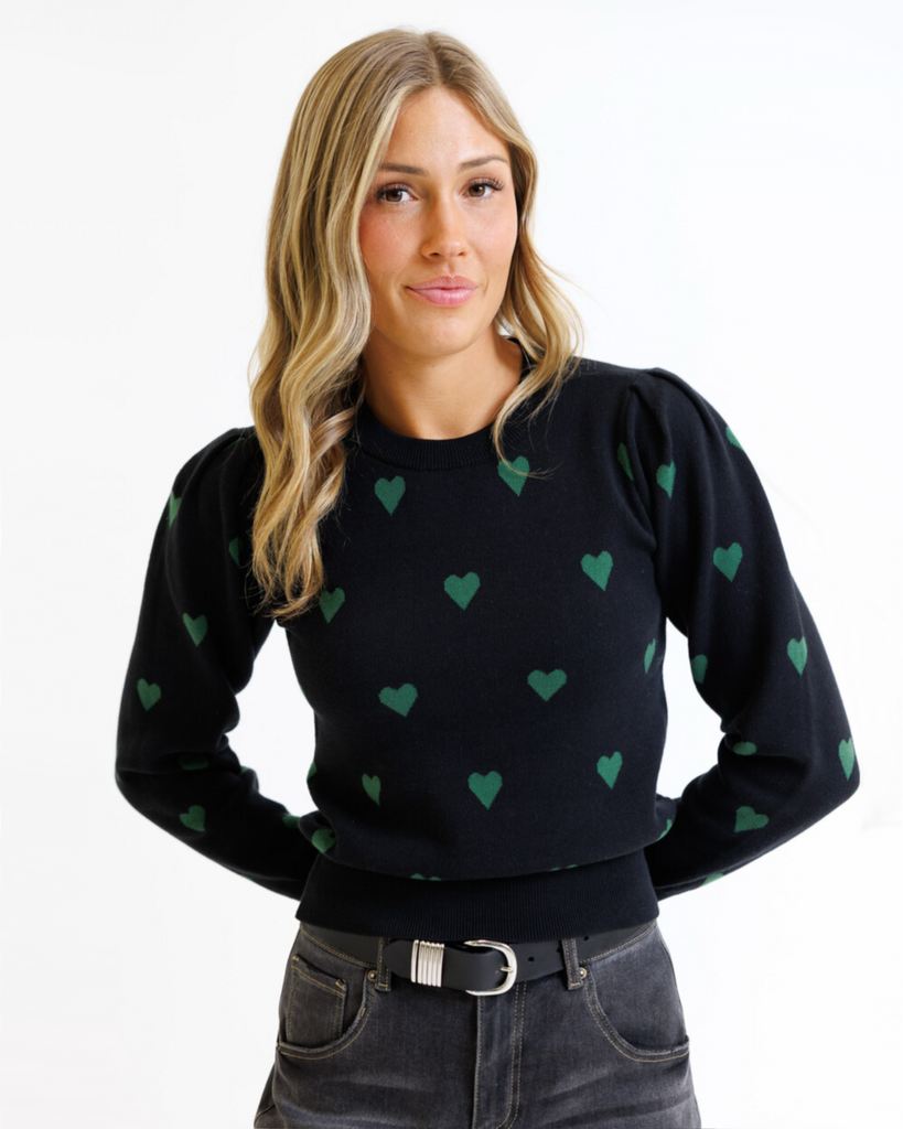 Woman wearing a black sweater with green heart patterns on a white background