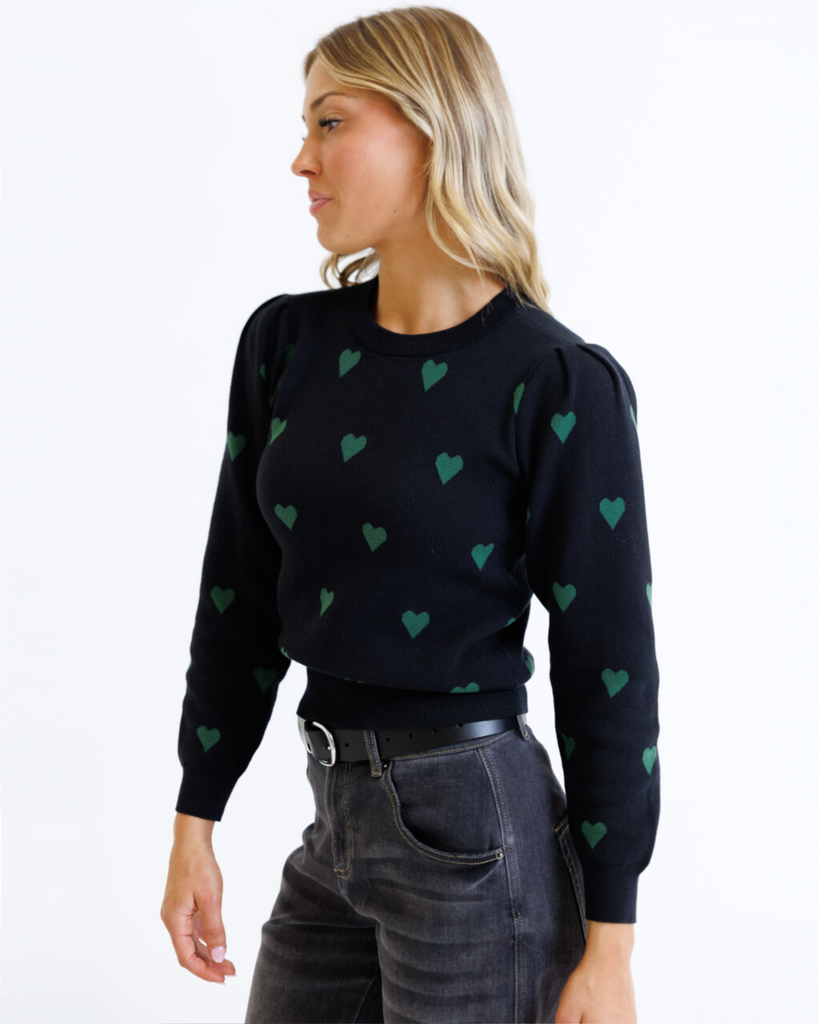 Woman wearing a black sweater with green heart patterns on a white background