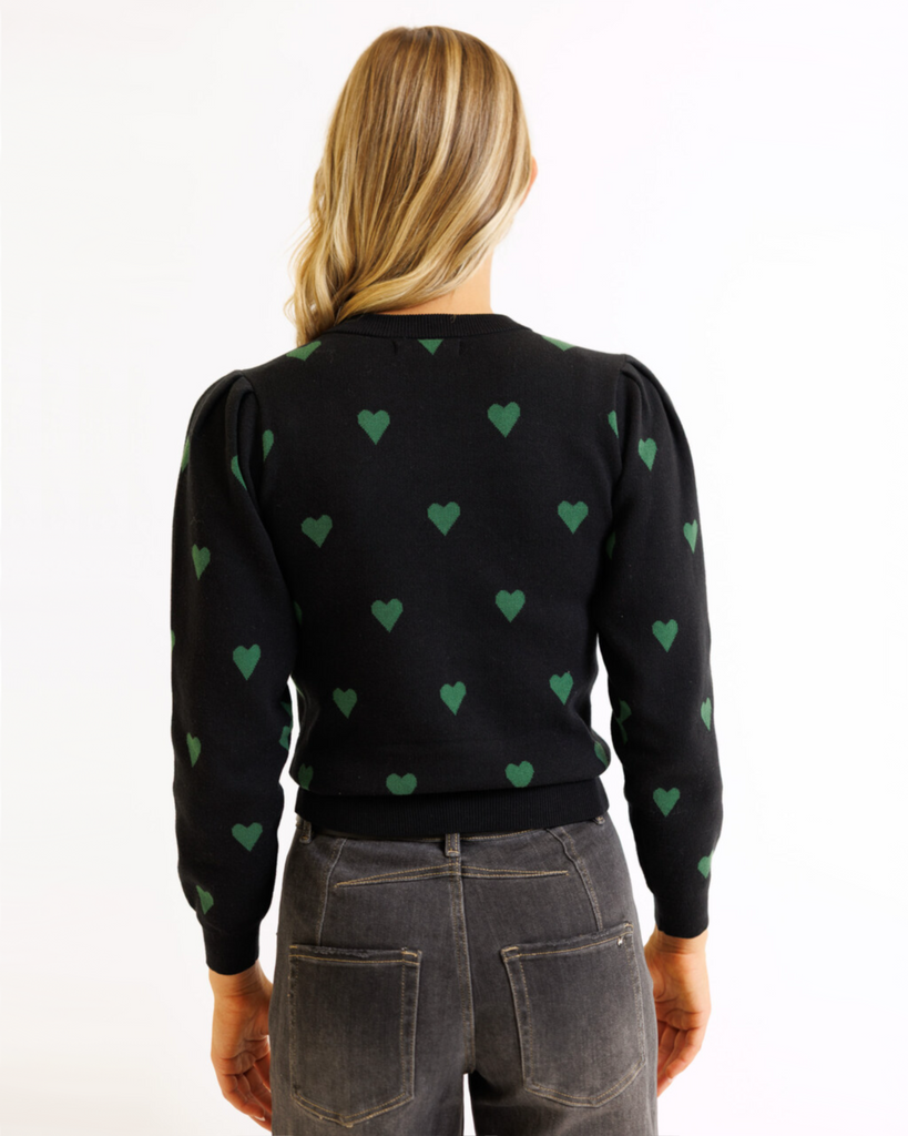 Person wearing a black sweater with green heart patterns on a white background