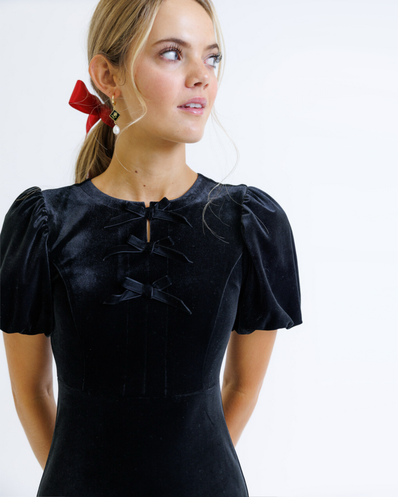 Woman wearing a black dress with puff sleeves against a white background