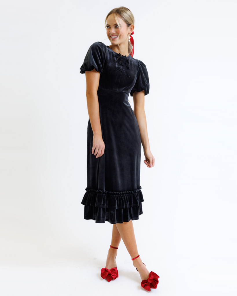 Woman wearing a black velvet dress with ruffled hem on a white background