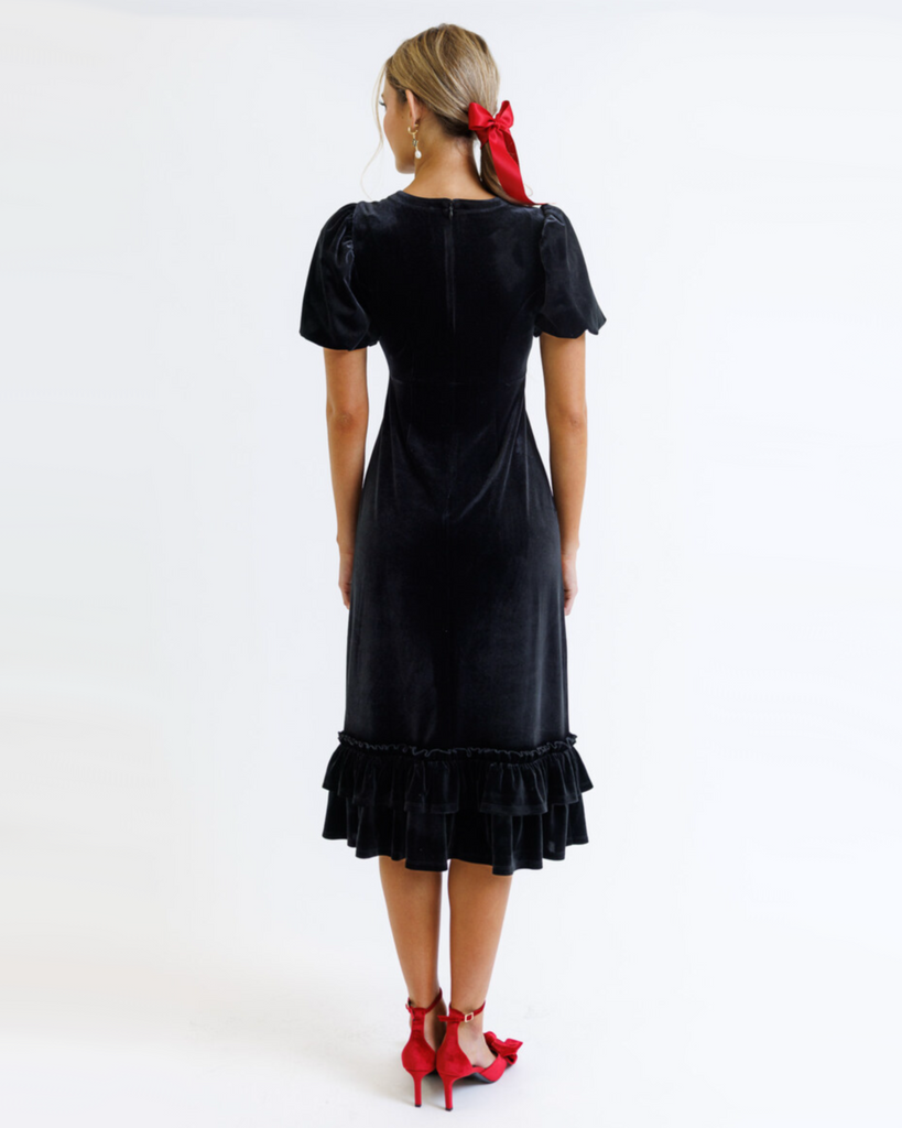 Woman wearing a black velvet dress with ruffled hem on a white background