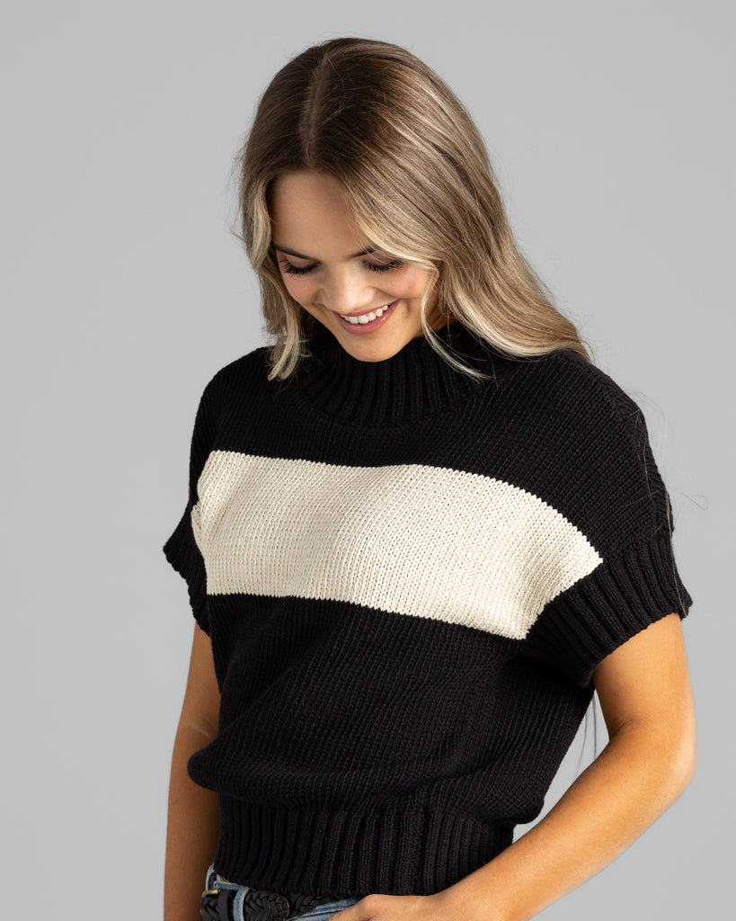 Model wearing a black with cream stripe short sleeve mock neck sweater.