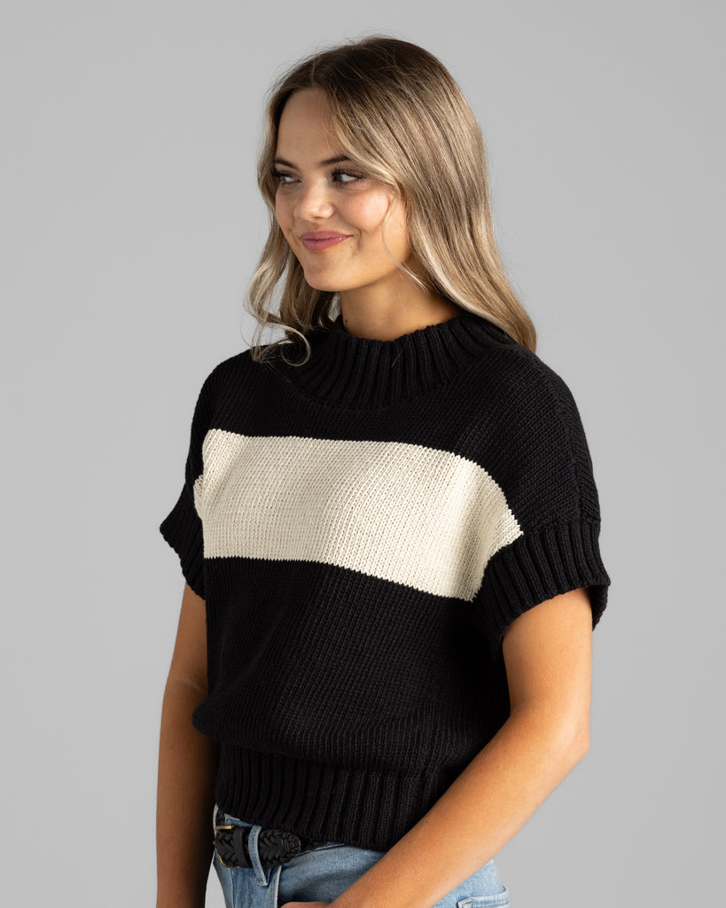 Model wearing a black with cream stripe short sleeve mock neck sweater.