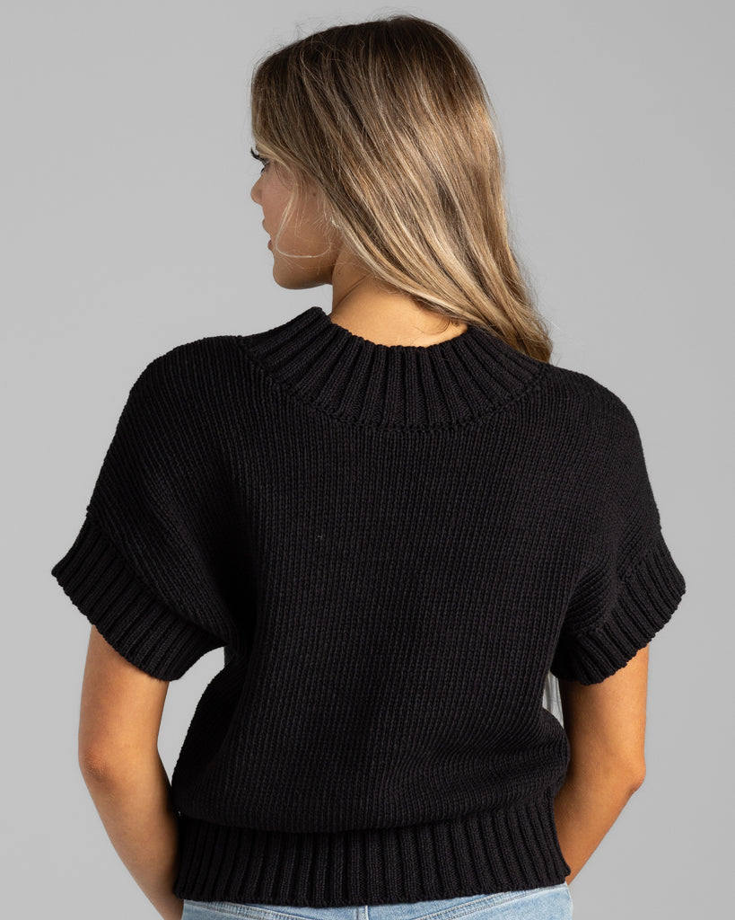 Model wearing a black with cream stripe short sleeve mock neck sweater.