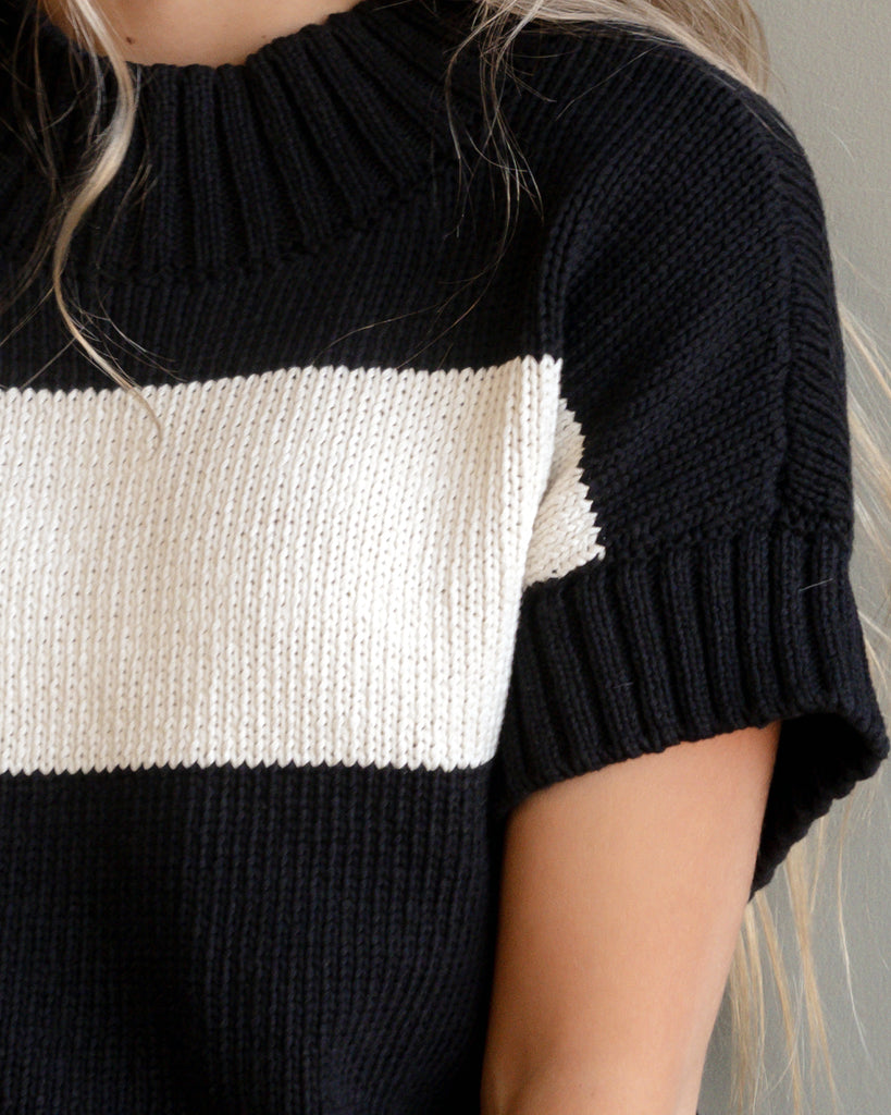 Model wearing a black with cream stripe short sleeve mock neck sweater.