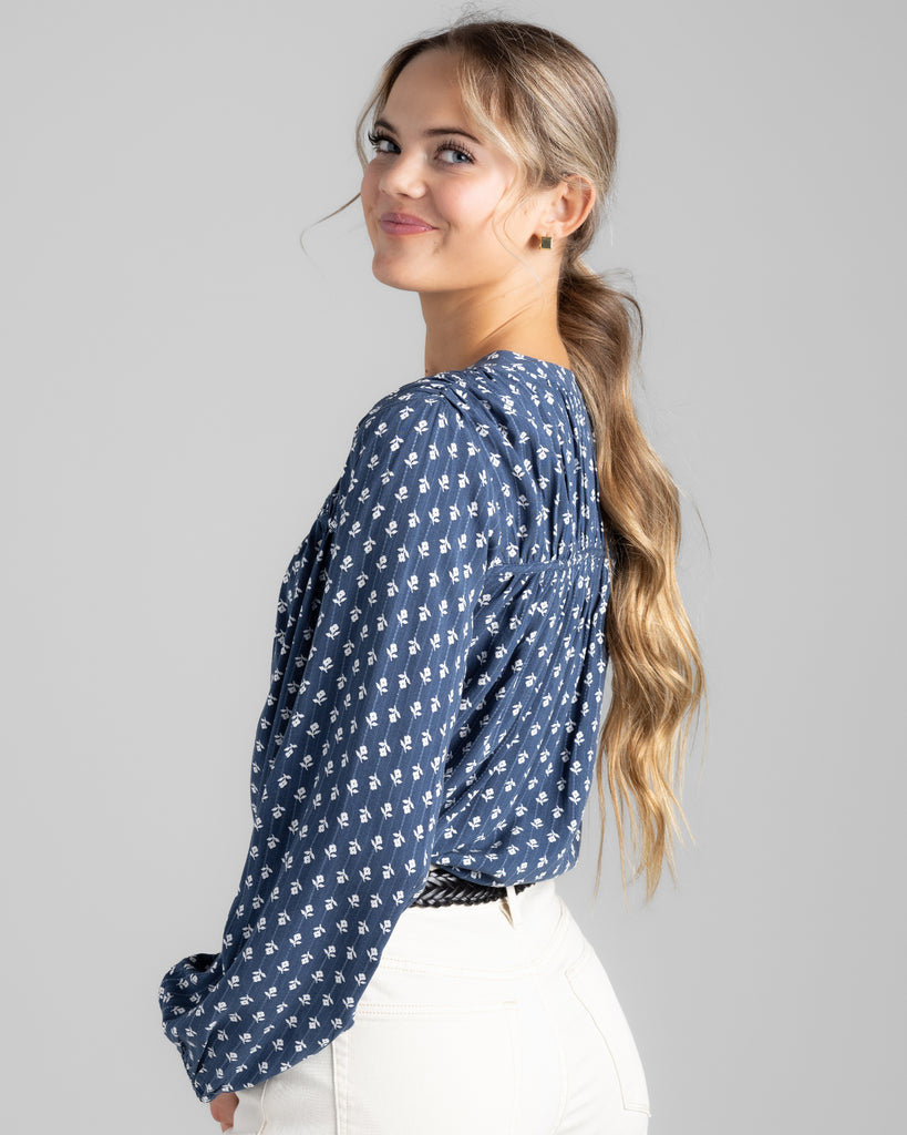 Model wearing a blue with white flowers long sleeve blouse with button details on top of bodice.