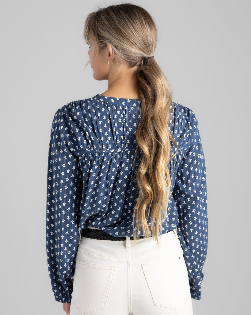 Model wearing a blue with white flowers long sleeve blouse with button details on top of bodice.