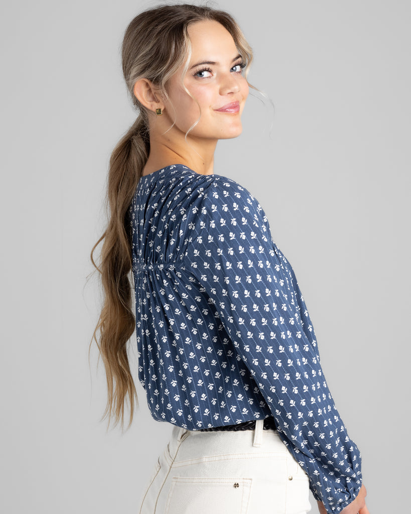 Model wearing a blue with white flowers long sleeve blouse with button details on top of bodice.