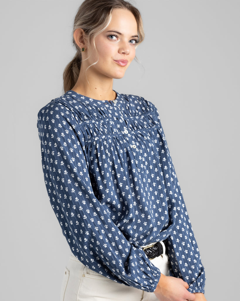 Model wearing a blue with white flowers long sleeve blouse with button details on top of bodice.