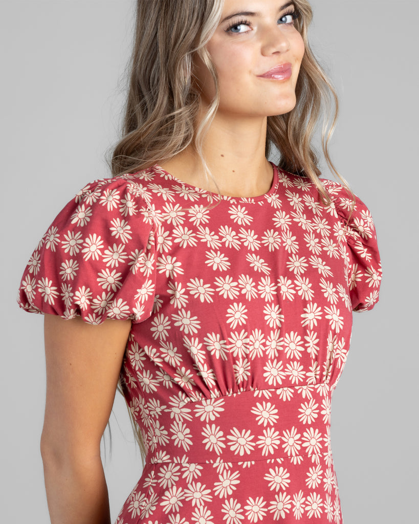 Model wearing a red with white daisy print, short sleeve midi length knit dress.