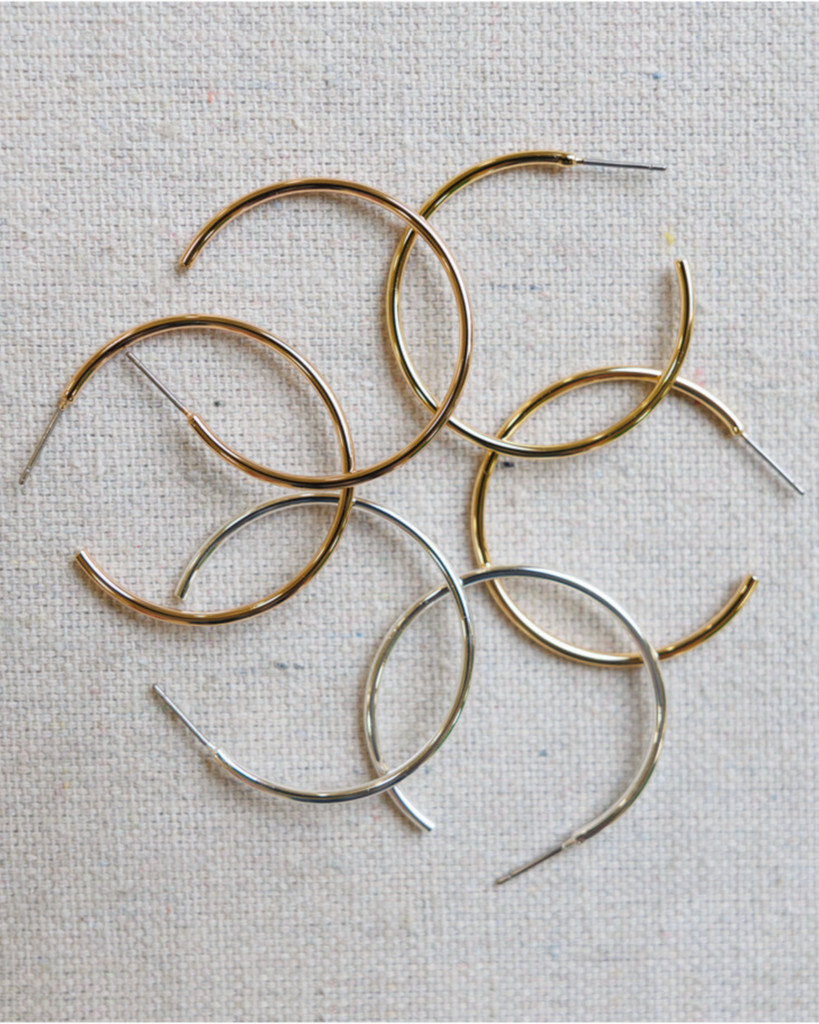 Gold and silver hoop earrings on a textured beige background