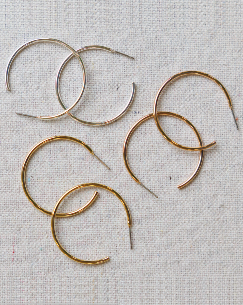 Silver and gold hoop earrings on a textured beige background