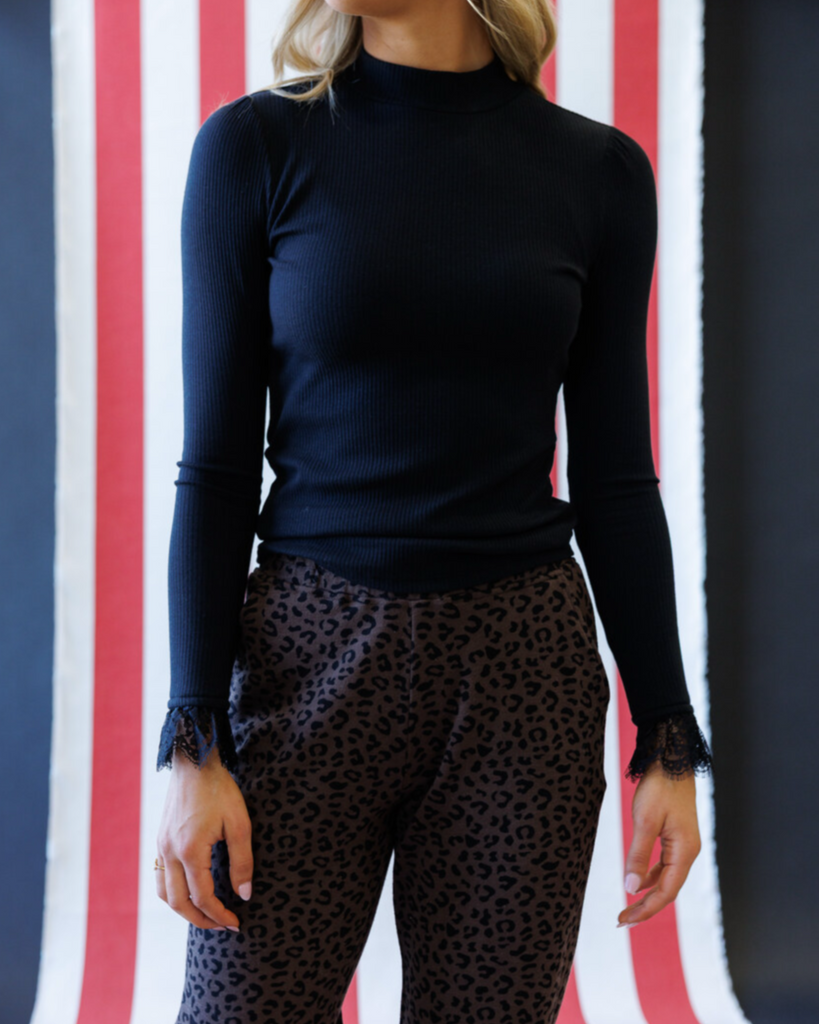 Woman wearing a black mock neck top and animal print pants in front of a striped background