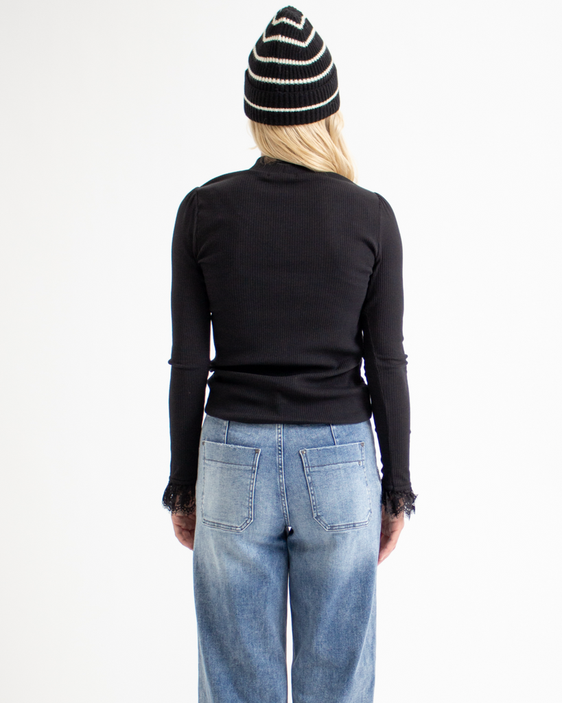 Woman wearing a black mock neck top with a black and white striped beanie in front of a white background