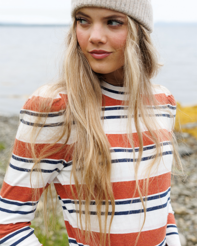 Woman wearing a striped mockneck shirt standing outside.