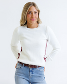 Woman wearing a white sweater with red accents and blue jeans on a white background