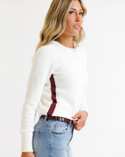 Woman wearing a white sweater with a red stripe and blue jeans on a white background