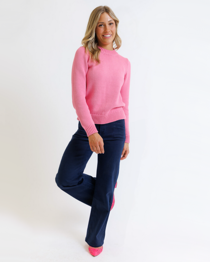 Woman wearing a pink sweater and navy pants on a white background