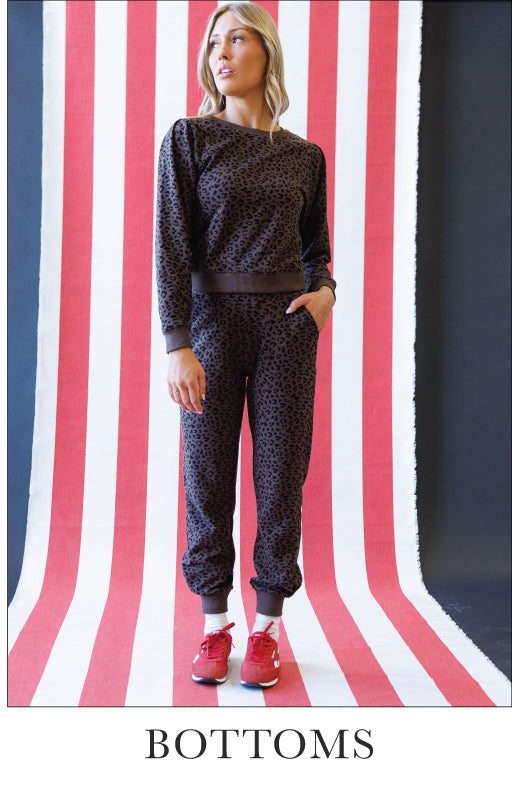 Woman wearing a matching animal print sweatshirt and sweatpants on a striped background. Bottom text says "Bottoms"