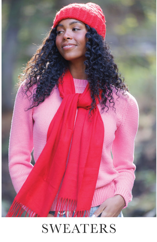 Woman wearing a pink sweater, red scarf, and hat outdoors. Bottom text says "Sweaters"