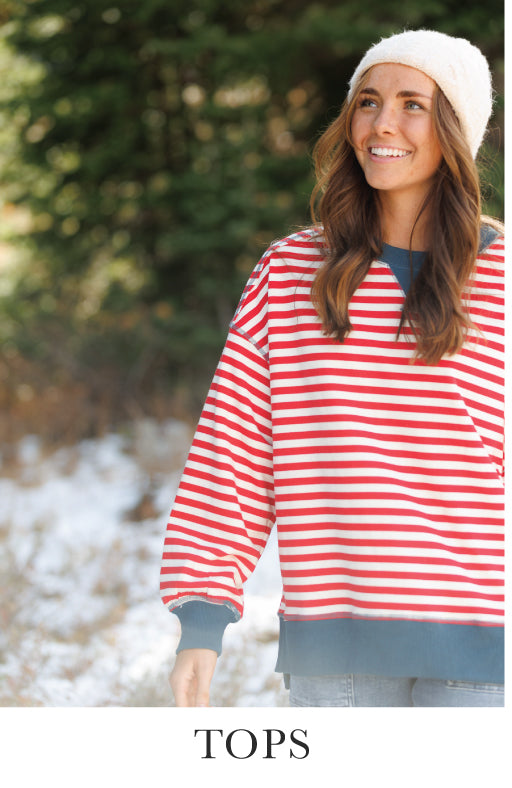 Woman wearing a red and white striped sweater outdoors with trees in the background. Bottom text says "Tops"