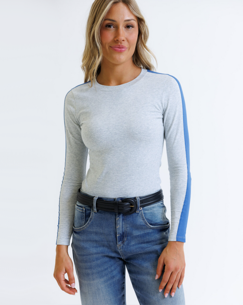 Woman wearing a gray long-sleeve top with blue accents and blue jeans on a white background