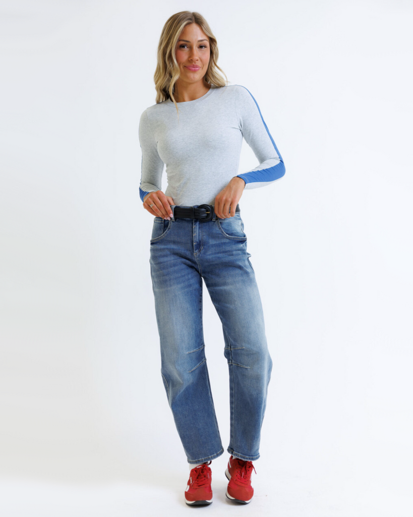 Woman wearing a gray long-sleeve top with blue accents and blue jeans on a white background