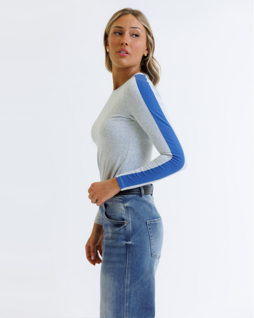 Woman wearing a gray long-sleeve top with blue accents and blue jeans on a white background