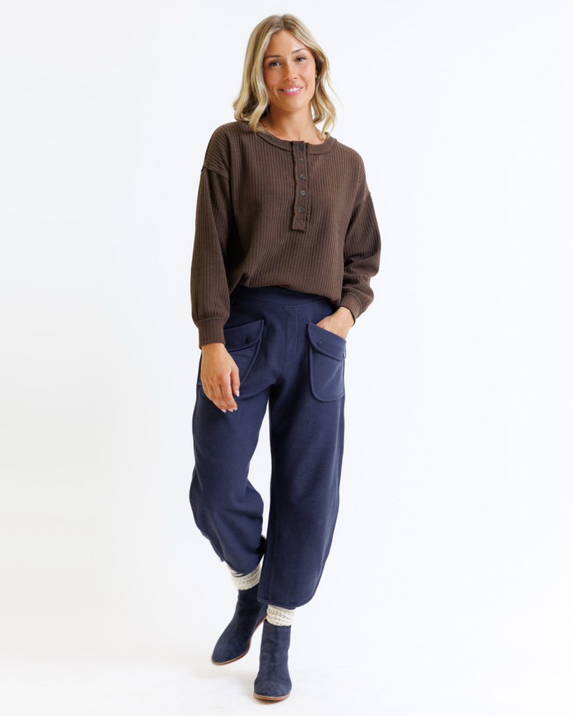 Woman wearing a brown long-sleeve top and blue pants on a white background