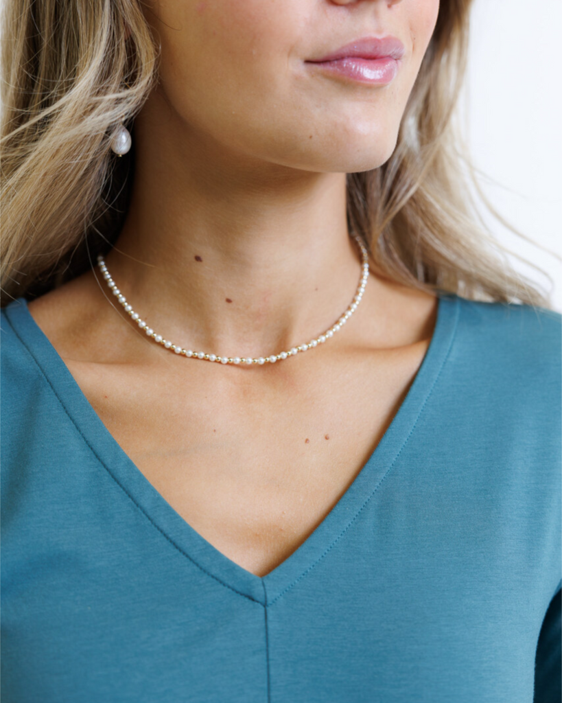 Woman wearing a pearl necklace, earrings, and a blue top