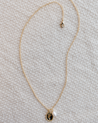 Gold necklace with a flower pendant and pearl charm on a textured beige surface