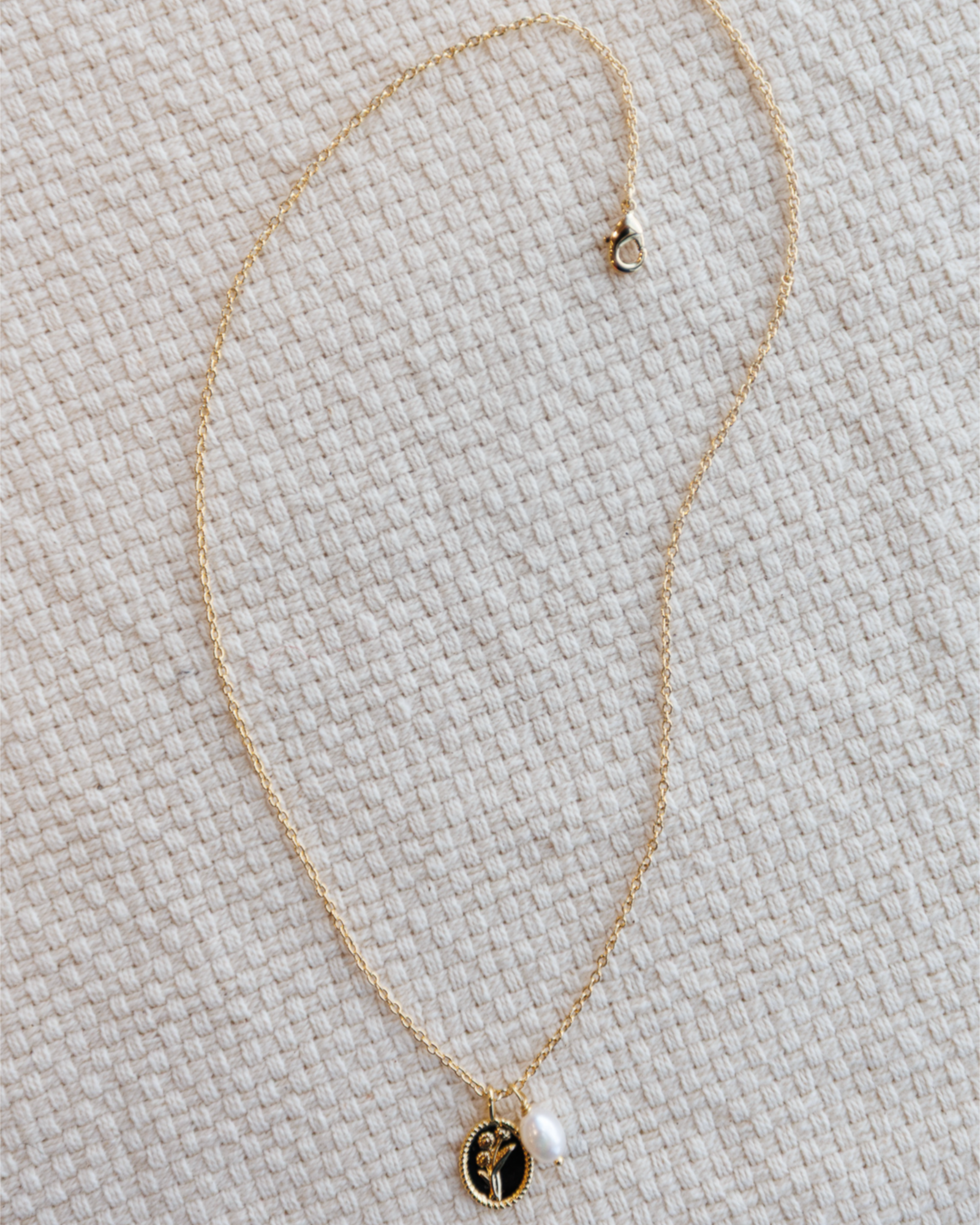 Gold necklace with a flower pendant and pearl charm on a textured beige surface