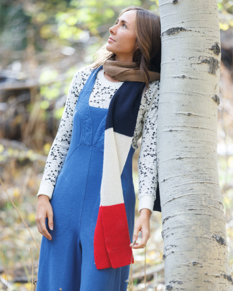 Woman in a blue jumpsuit leaning against a tree in a natural setting
