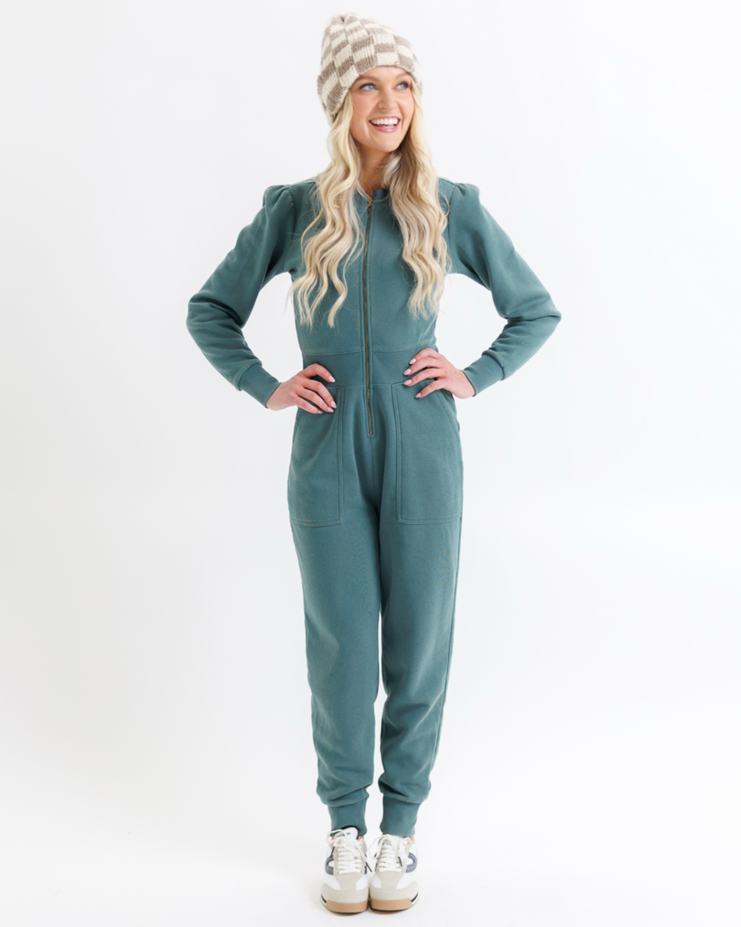 Woman wearing a teal jumpsuit and white sneakers on a white background