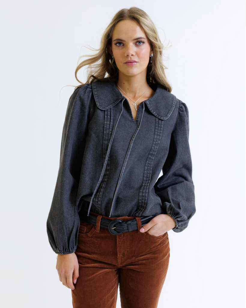 Woman wearing a dark denim shirt and brown pants on a white background