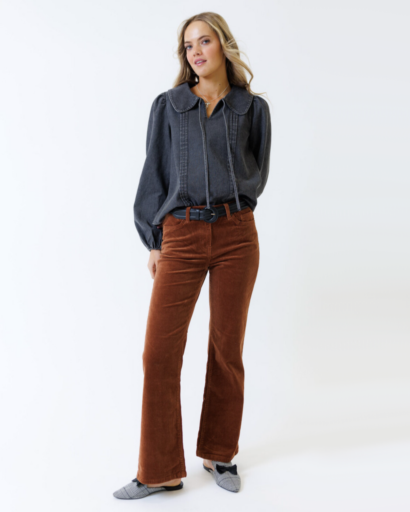 Woman wearing a dark denim shirt and brown pants on a white background