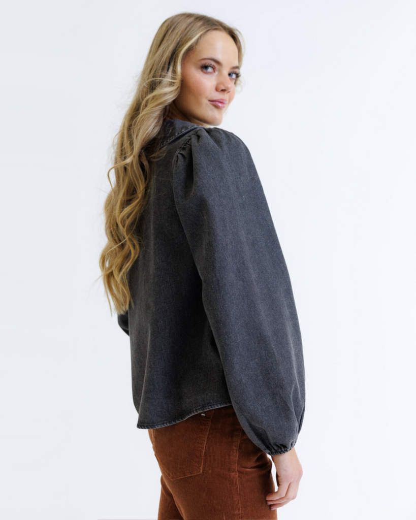 Woman wearing a dark denim shirt and brown pants on a white background