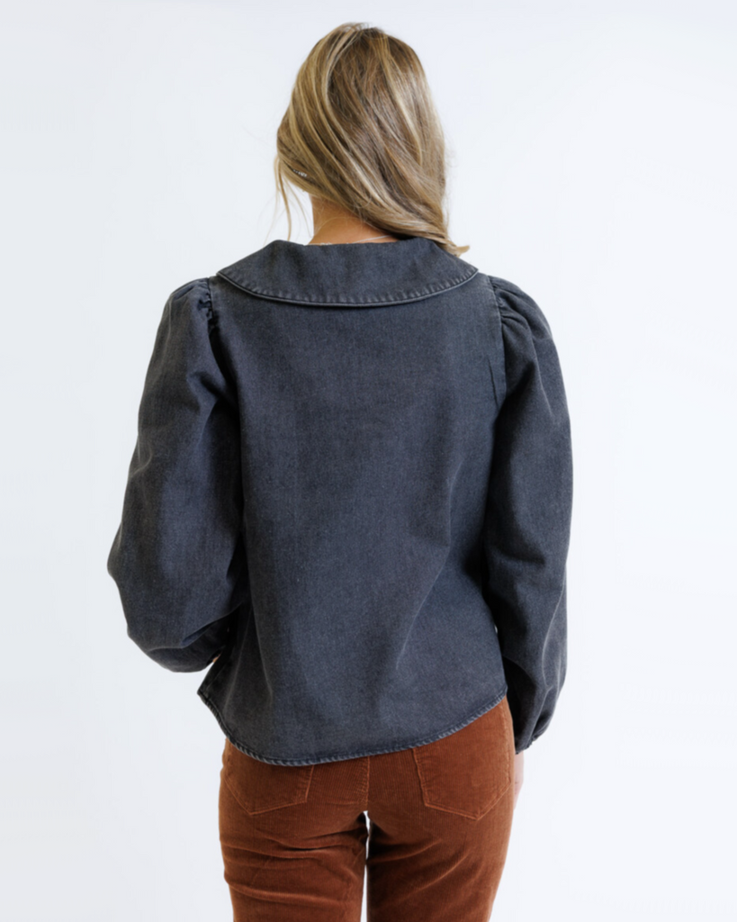 Woman wearing a dark denim shirt and brown pants on a white background