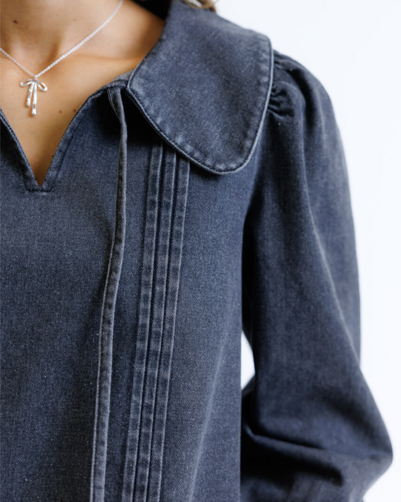 Woman wearing a dark denim shirt and brown pants on a white background