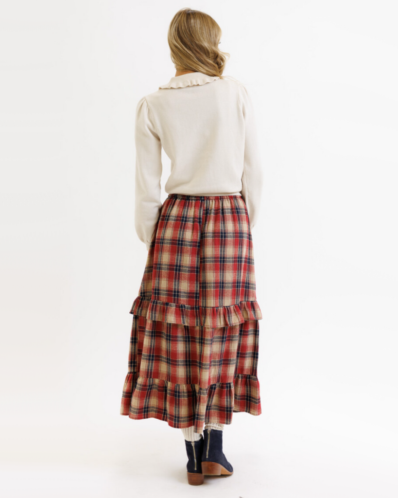Woman wearing a cream colored sweater and plaid print maxi skirt on a white background