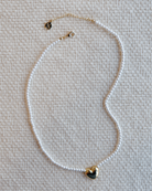 Pearl necklace with a heart-shaped pendant on a textured beige surface