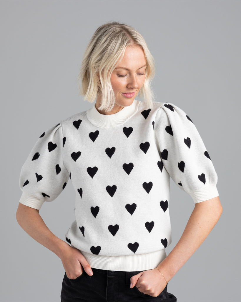 Model wearing a white with black hearts short sleeve crew neck sweater.