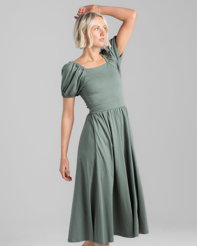 Model wearing a sage green, short puffed sleeve, square neck midi length dress with pockets.