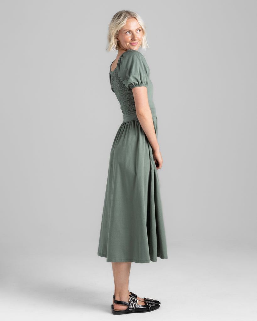 Model wearing a sage green, short puffed sleeve, square neck midi length dress with pockets.