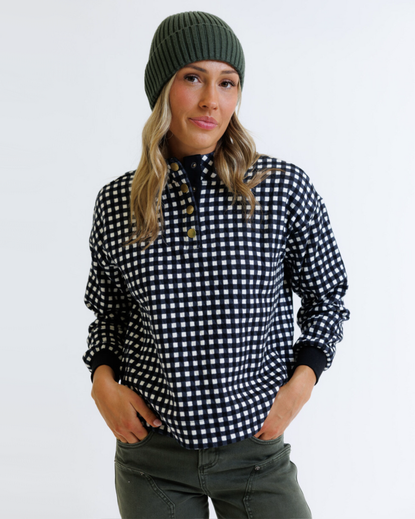 Woman wearing a black and white checkered pullover with a green beanie on a white background