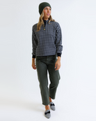 Woman wearing a black and white checkered pullover, green beanie, and green pants on a white background