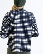 Woman wearing a black and white checkered pullover with a green beanie on a white background