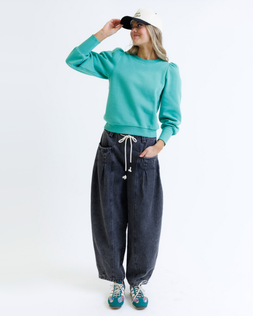Woman wearing a teal sweatshirt and black jeans on a white background